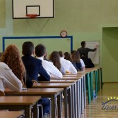 Uczniowie zdający egzamin siedzą w ławkach w sali gimnastycznej